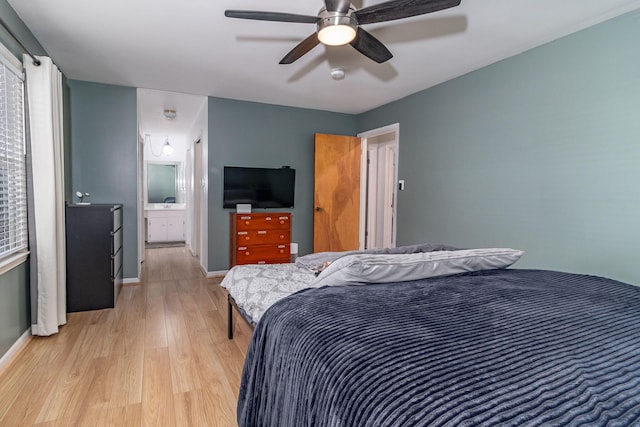 bedroom with ensuite bath, light wood-style flooring, multiple windows, and baseboards