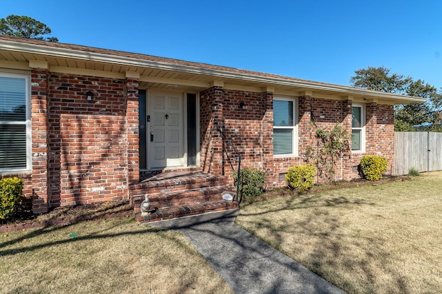 doorway to property featuring a yard, fence, and brick siding