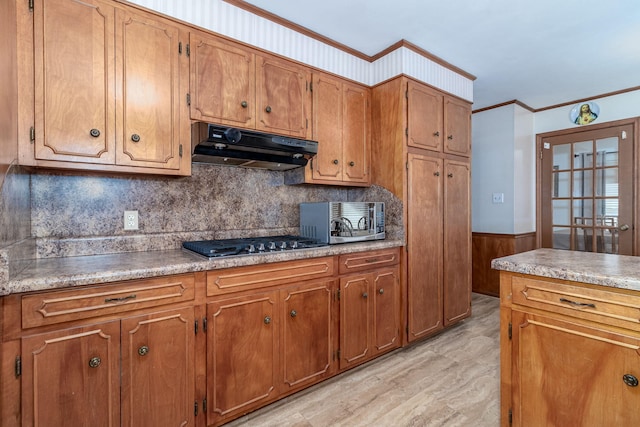 kitchen featuring a wainscoted wall, ornamental molding, under cabinet range hood, stainless steel appliances, and brown cabinetry