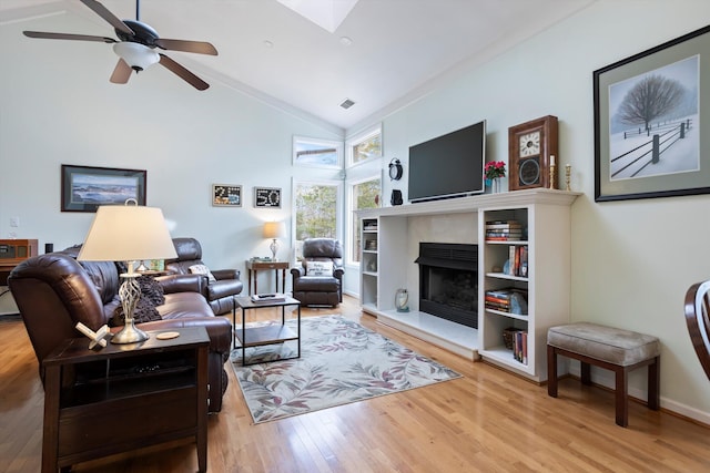 living area with a skylight, visible vents, wood finished floors, high vaulted ceiling, and a high end fireplace