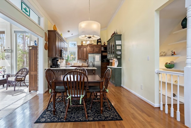 dining area featuring vaulted ceiling, light wood finished floors, crown molding, and baseboards