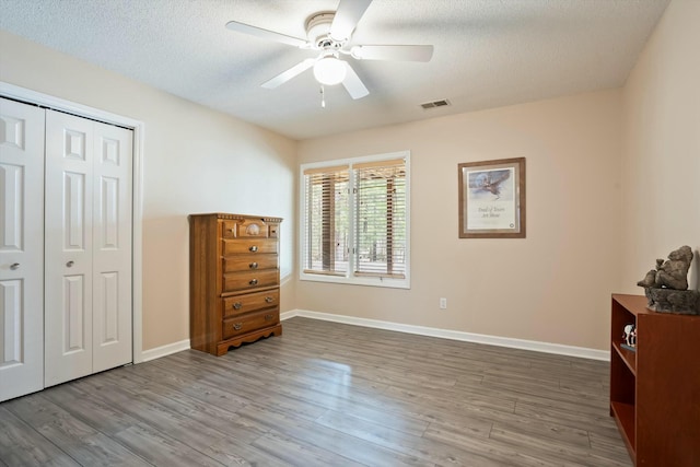 unfurnished bedroom featuring a closet, visible vents, a textured ceiling, wood finished floors, and baseboards