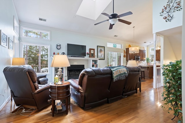 living room with a skylight, a fireplace, visible vents, ceiling fan, and light wood-type flooring