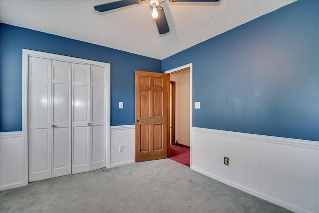 unfurnished bedroom with ceiling fan, light colored carpet, a textured ceiling, and a closet