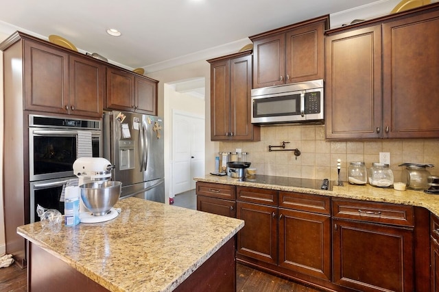 kitchen featuring crown molding, stainless steel appliances, a center island, light stone counters, and decorative backsplash