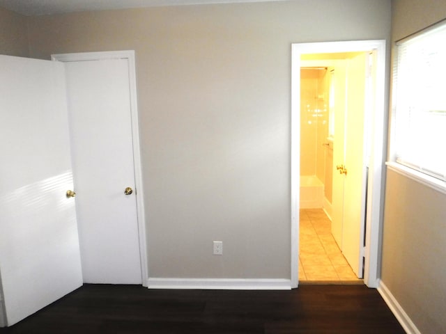 unfurnished bedroom featuring connected bathroom, hardwood / wood-style flooring, and multiple windows