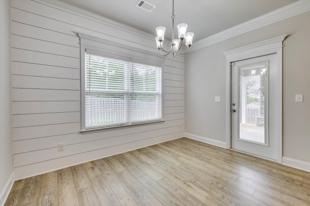 spare room featuring a notable chandelier, wood walls, light wood-type flooring, and crown molding