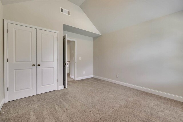 unfurnished bedroom with a closet, light colored carpet, and lofted ceiling