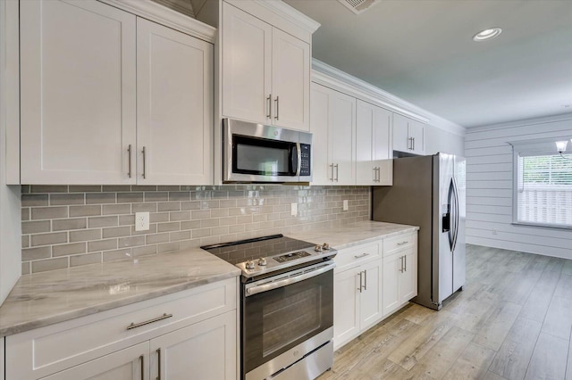 kitchen with light wood-type flooring, appliances with stainless steel finishes, tasteful backsplash, light stone counters, and white cabinetry