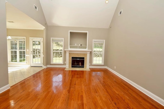 unfurnished living room featuring a tiled fireplace, high vaulted ceiling, and light hardwood / wood-style flooring