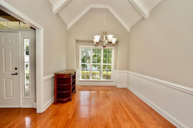 unfurnished dining area with a healthy amount of sunlight, lofted ceiling with beams, wood-type flooring, and a notable chandelier