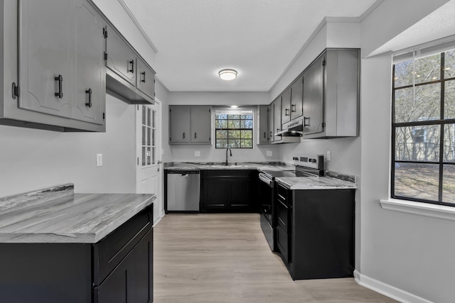 kitchen featuring a sink, under cabinet range hood, appliances with stainless steel finishes, light wood finished floors, and light countertops