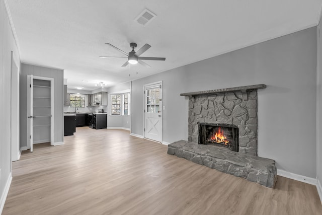 unfurnished living room with baseboards, visible vents, light wood finished floors, a fireplace, and ceiling fan