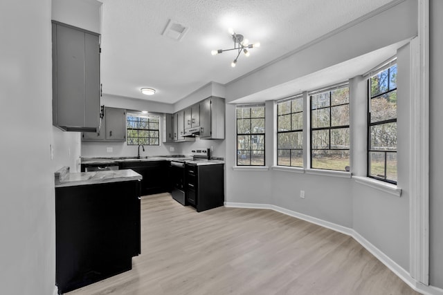 kitchen with electric range, gray cabinets, light countertops, a textured ceiling, and light wood-type flooring