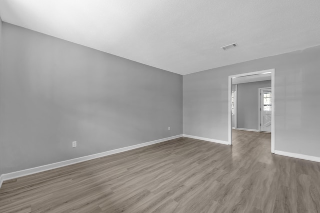 unfurnished room with a textured ceiling, wood finished floors, visible vents, and baseboards