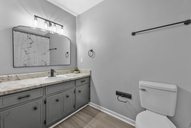 bathroom with vanity, toilet, wood finished floors, and baseboards