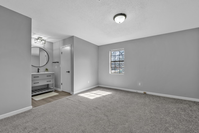 unfurnished bedroom with a sink, baseboards, a textured ceiling, and carpet flooring