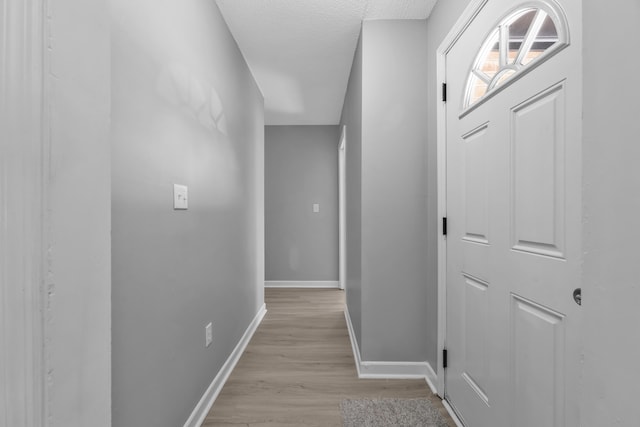 hall featuring baseboards, light wood-style floors, and a textured ceiling