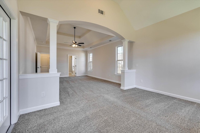 carpeted spare room with visible vents, a raised ceiling, a ceiling fan, arched walkways, and ornate columns