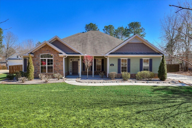 view of front of property featuring stone siding, a front lawn, a shingled roof, and fence