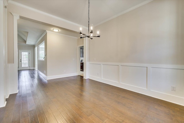 empty room with dark wood-style floors, crown molding, a notable chandelier, and a decorative wall