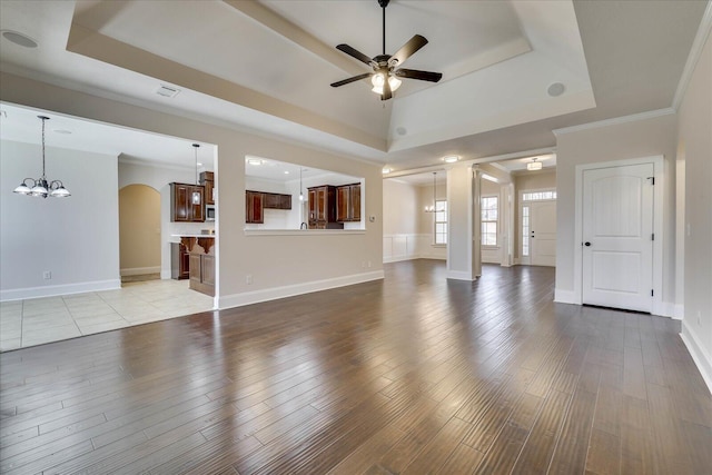 unfurnished living room featuring ceiling fan with notable chandelier, a tray ceiling, arched walkways, and wood finished floors