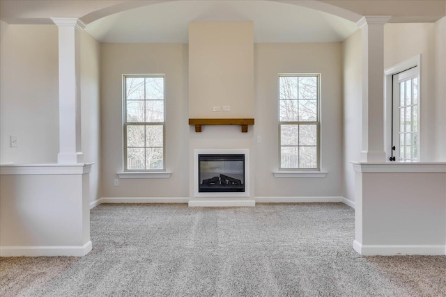 unfurnished living room featuring baseboards, arched walkways, a glass covered fireplace, carpet flooring, and ornate columns