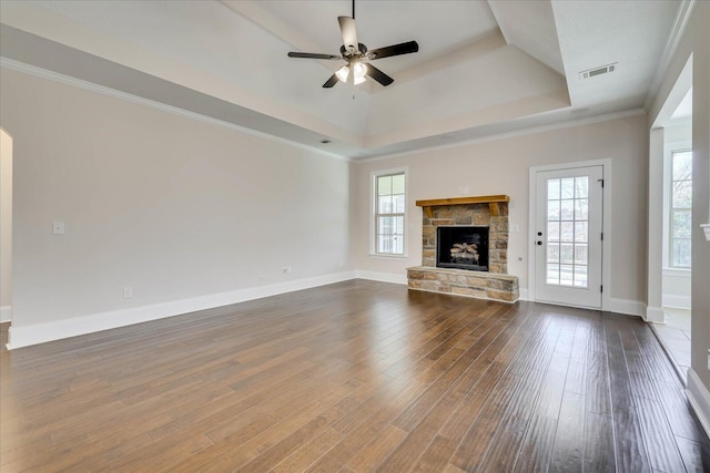 unfurnished living room with ceiling fan, a stone fireplace, wood finished floors, visible vents, and a tray ceiling