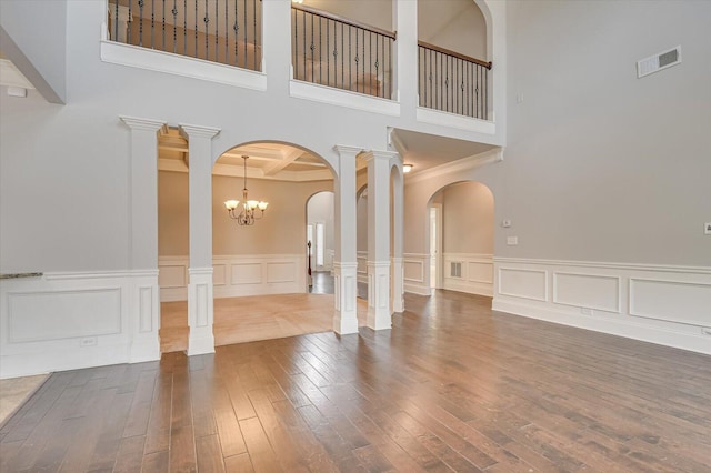 unfurnished room featuring dark wood-type flooring, an inviting chandelier, and ornate columns