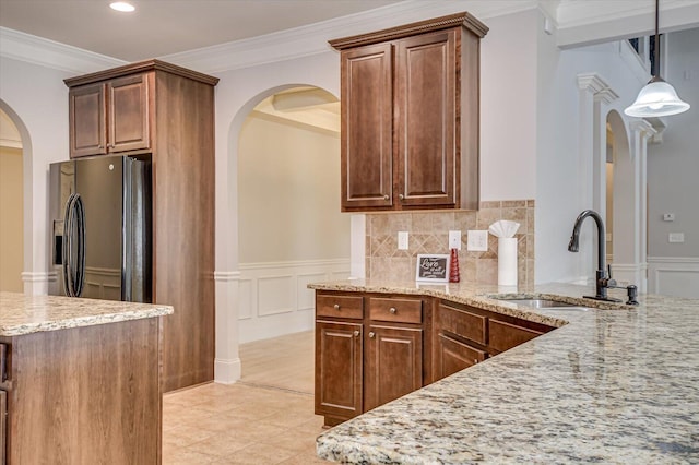 kitchen with hanging light fixtures, light stone countertops, black fridge with ice dispenser, crown molding, and sink