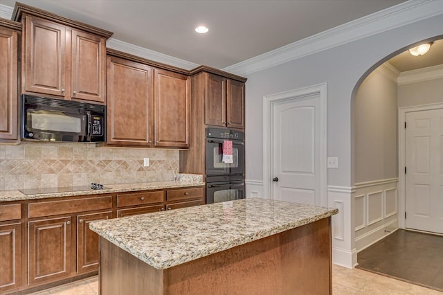 kitchen with a center island, black appliances, tasteful backsplash, light stone counters, and crown molding