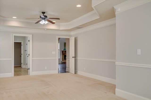 empty room with ceiling fan, crown molding, a raised ceiling, and light colored carpet