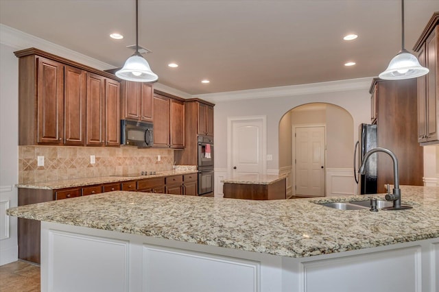 kitchen with sink, decorative light fixtures, crown molding, black appliances, and an island with sink