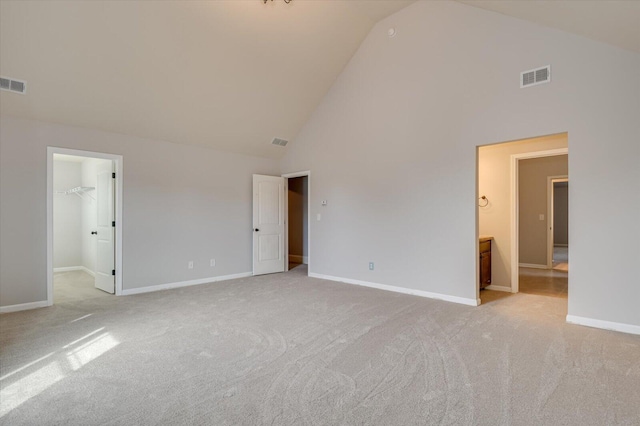 unfurnished bedroom with high vaulted ceiling, a walk in closet, and light colored carpet