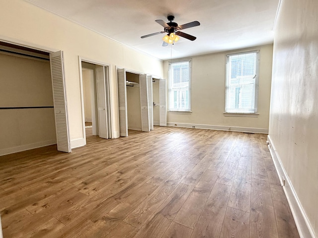 unfurnished bedroom featuring hardwood / wood-style flooring, two closets, and ceiling fan