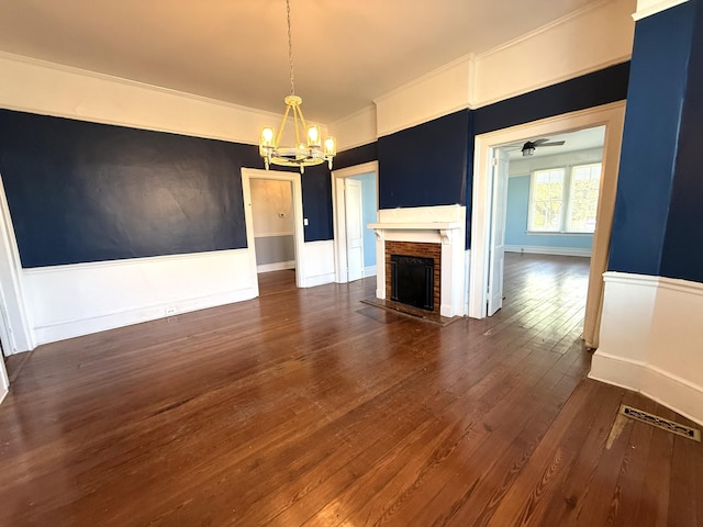 unfurnished living room featuring a notable chandelier, crown molding, dark hardwood / wood-style floors, and a brick fireplace