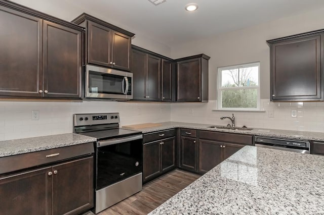 kitchen featuring stainless steel appliances, a sink, dark brown cabinets, dark wood-type flooring, and light stone counters