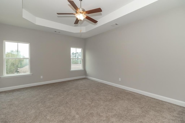 empty room featuring a tray ceiling, carpet floors, ceiling fan, and baseboards