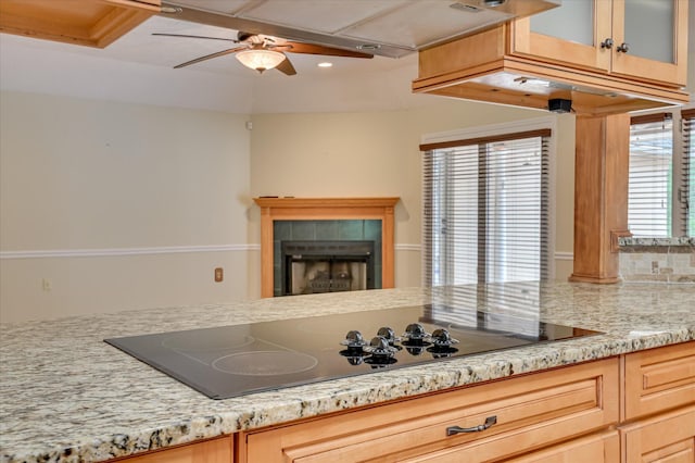 3129 Goolsby Rd, Blythe, GA 30805 - kitchen featuring black electric cooktop, a fireplace, a ceiling fan, light stone counters, and glass insert cabinets