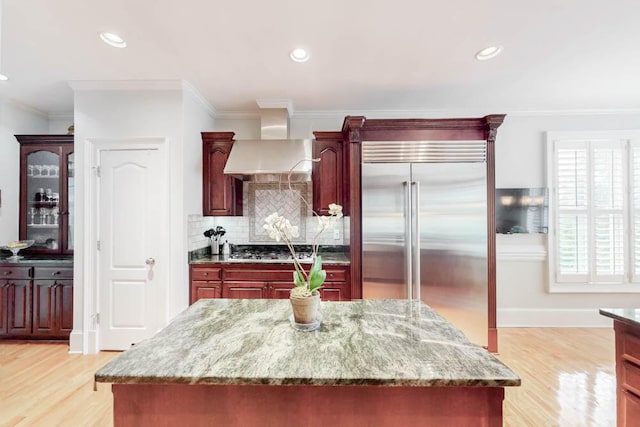 114 Altamaha Dr, North Augusta, SC 29841 - kitchen with appliances with stainless steel finishes, wall chimney range hood, reddish brown cabinets, crown molding, and light wood-type flooring