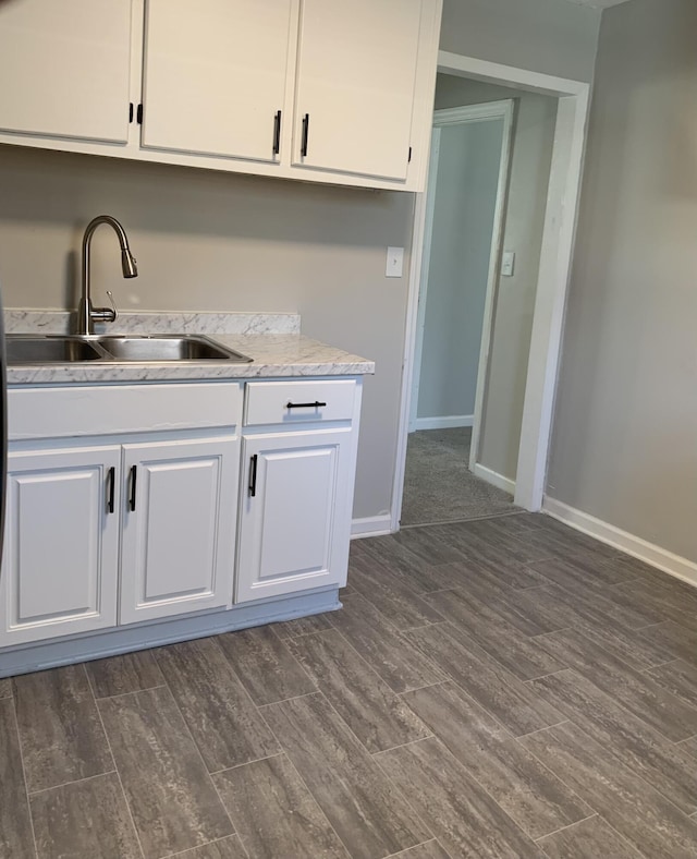 kitchen with white cabinetry, sink, dark wood-type flooring, and light stone counters