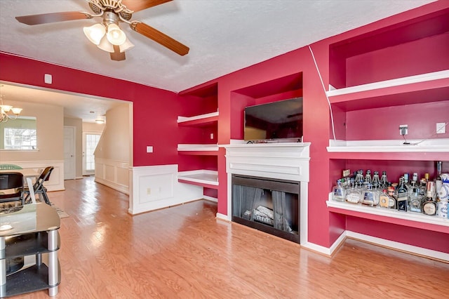 living room with ceiling fan with notable chandelier, wood-type flooring, built in shelves, and a textured ceiling