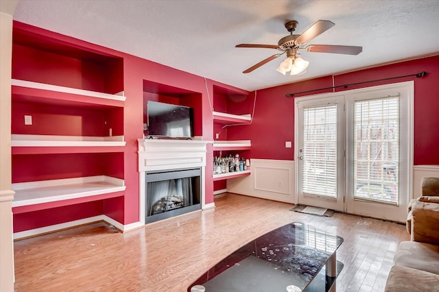 living room with hardwood / wood-style flooring, ceiling fan, built in features, and a textured ceiling