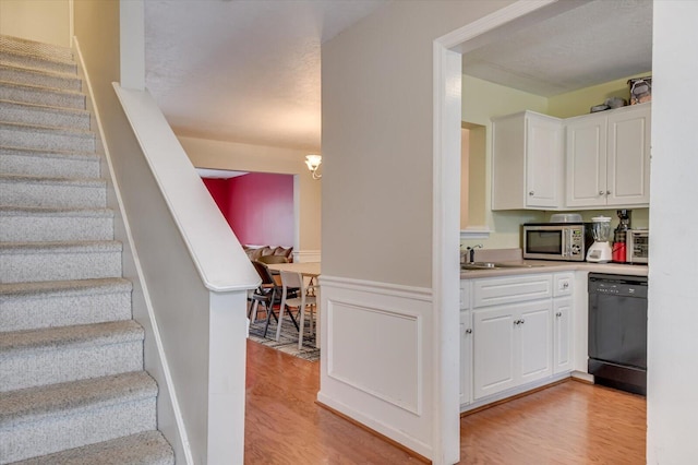 interior space featuring decorative light fixtures, dishwasher, light hardwood / wood-style flooring, and white cabinets