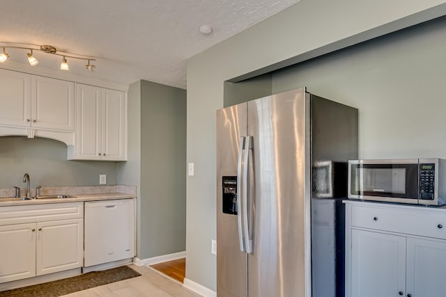 kitchen with light countertops, appliances with stainless steel finishes, a sink, and white cabinetry