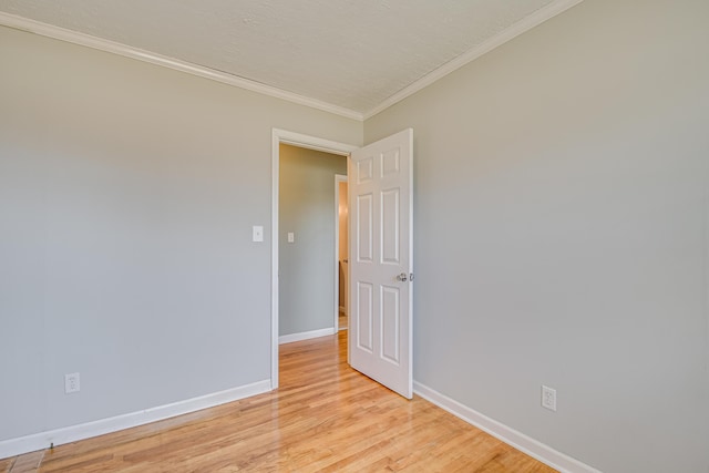 empty room featuring crown molding, light wood-type flooring, and baseboards