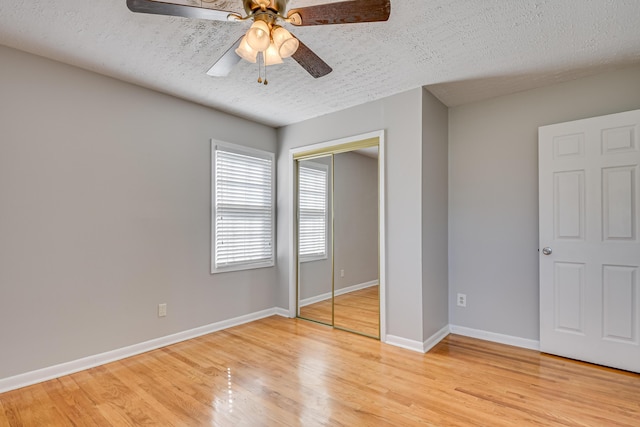 unfurnished bedroom with light wood finished floors, baseboards, a ceiling fan, a textured ceiling, and a closet