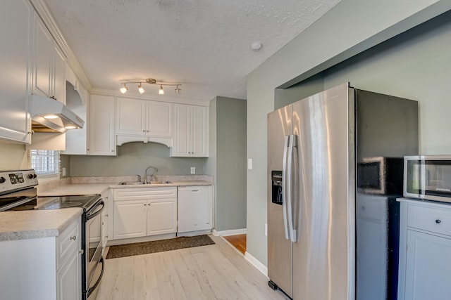 kitchen featuring appliances with stainless steel finishes, light countertops, under cabinet range hood, white cabinetry, and a sink