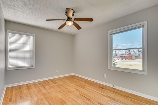 empty room with ceiling fan, a textured ceiling, baseboards, and wood finished floors