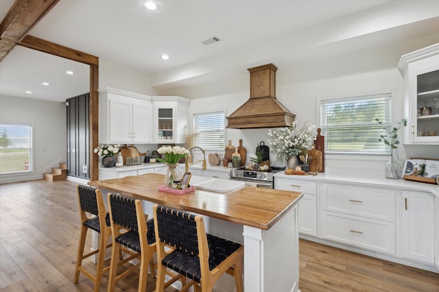 1513 Paris Ave, Swainsboro, GA 30401 - kitchen with custom range hood, stainless steel electric stove, white cabinetry, glass insert cabinets, and butcher block countertops